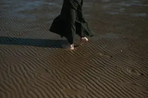 Person walking barefoot on the sand – grounding movement that helps reset and calm the nervous system.